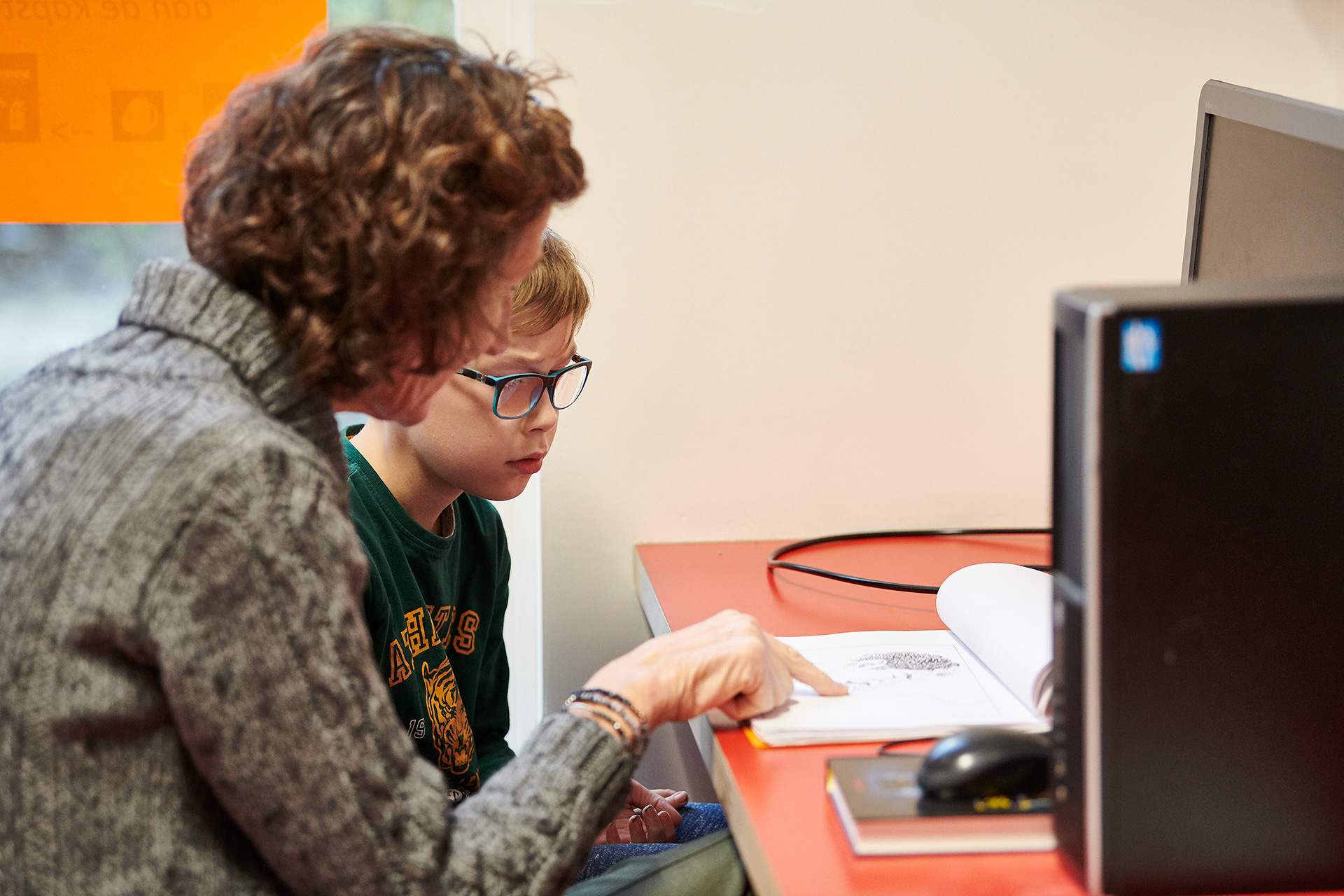Leerkracht legt iets uit aan leerling achter de computer